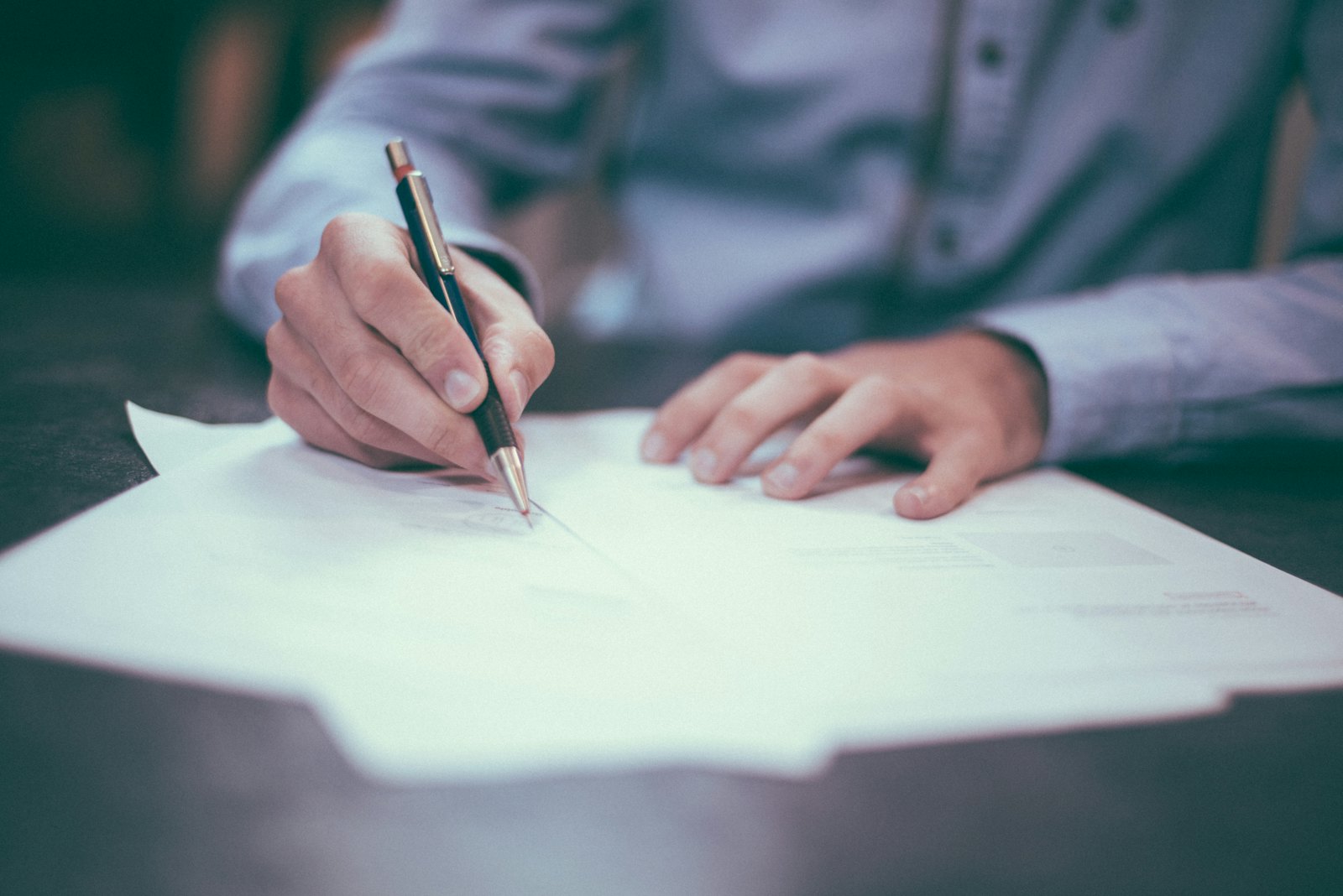 Persona firmando documentos con un bolígrafo sobre la mesa de una oficina